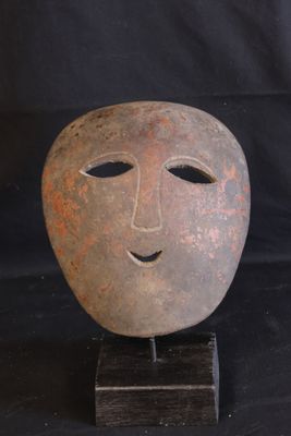 a clay mask on a wooden stand on a black background