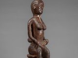 a wooden statue of a woman sitting on a stool