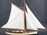 maquette en bois d'un voilier aux voiles blanches, posée sur un socle