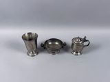 two silver cups and a silver teapot on a white surface