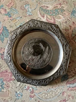une assiette en argent ornée d'un oiseau, posée sur une nappe à motifs floraux