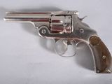 revolver argenté avec une crosse en bois, posé sur une surface blanche