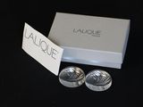 deux paires de menottes en argent, présentées dans une boîte blanche posée sur un fond noir
