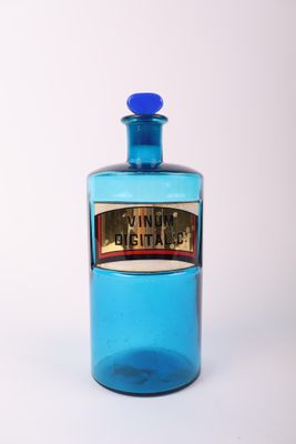 une bouteille en verre bleue ornée d'une étiquette dorée, posée sur une surface blanche