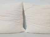 two white pillows sitting on top of a white table next to a wall