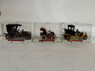 Trois modèles réduits de voitures anciennes sont exposés dans des vitrines posées sur une table