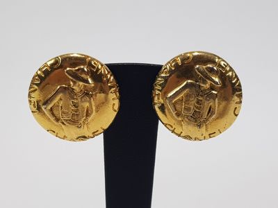a pair of gold earrings on a black stand