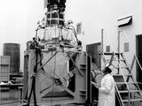 une vieille photo en noir et blanc montrant un homme en blouse de laboratoire debout à côté d'une machine