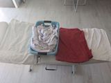 a bed with a red blanket and a blue suitcase with clothes on it
