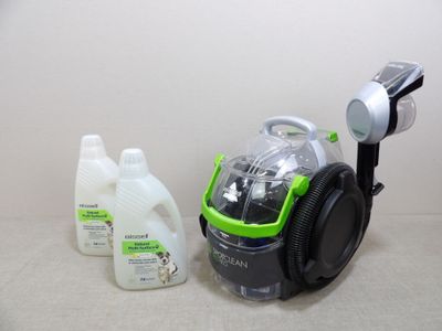 un aspirateur vert et noir à côté d'une bouteille de produit nettoyant