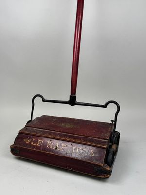 une vieille brosse de toilettes rouge et noire posée sur une caisse en bois