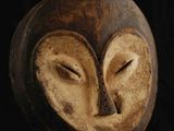 un masque en bois posé sur un socle, sur fond noir