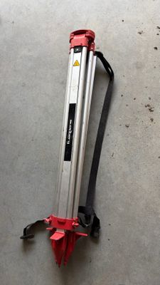 a close up of a tripod on a concrete floor with a red handle