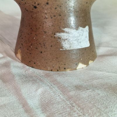 un vase marron posé sur une table recouverte d'une nappe blanche