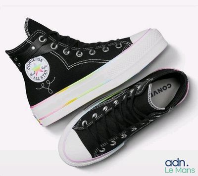 Des baskets Converse noires aux semelles arc-en-ciel sont posées sur une surface blanche