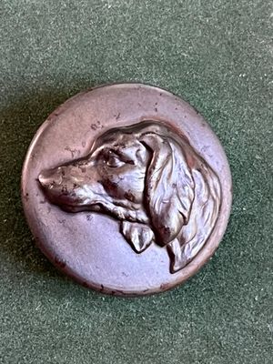 un bouton en métal représentant un chien, sur un fond vert