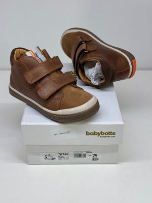 des chaussures de bébé en cuir marron avec des bandes Velcro, posées sur une boîte blanche