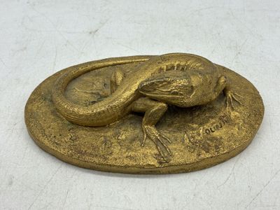 plaque en laiton surmontée d'un lézard, posée sur un fond blanc