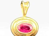 a close up of a gold pendant with a pink stone