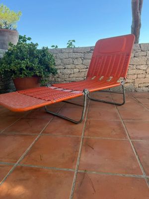 an orange lounge chair sitting on a patio with a potted plant in the background