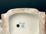 a hand holding a small white vase with a hole in it