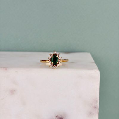 un gros plan d'une bague sertie d'une émeraude verte et de diamants, posée sur un bloc de marbre blanc