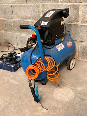 a blue air compressor sitting on the ground next to a brick wall