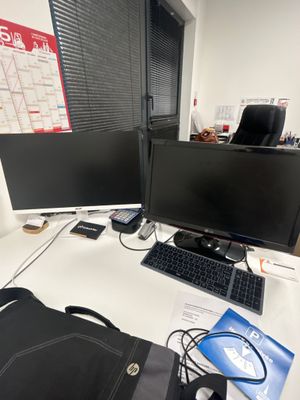 un sac noir posé sur un bureau, à côté de deux écrans d'ordinateur