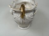 a white vase with a gold handle on a white table