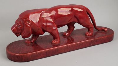 statue d'un lion rouge posée sur un socle en bois, sur fond gris