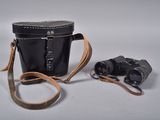 un sac noir muni d'une bandoulière marron, avec une paire de jumelles posée à côté