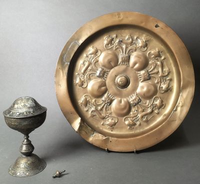a gold plate with a flower design on it next to a silver cup