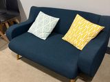 a blue couch with two pillows on it in the corner of a room