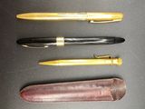 three pens are lined up on a black surface with a leather case
