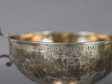 an old silver bowl with a handle on a gray surface