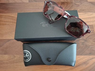 Lunettes de soleil Ray-Ban dans leur boîte et leur étui, posées sur un parquet