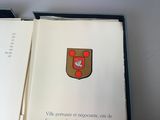 un livre ouvert sur lequel figure un blason