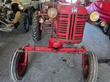 a red tractor sitting in a garage with other antique cars