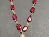 a close up of a necklace with a red and green bead