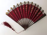 éventail chinois rouge orné de motifs dorés et d'un pompon rouge