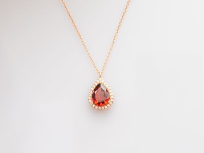 a gold necklace with a red tear shaped stone on a white background