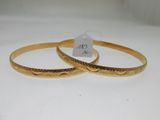 two gold bracelets with engraved designs on them on a white surface