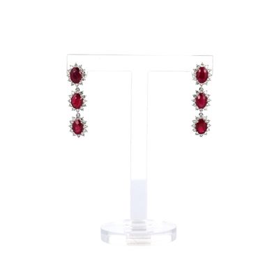 une paire de boucles d'oreilles en rubis et diamants posée sur un socle en acrylique transparent