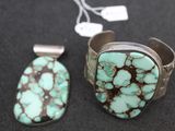 two pieces of turquoise and silver jewelry on a black surface