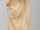 a statue of a woman sitting on a table next to a vase