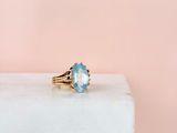 a gold ring with a blue topaz stone on top of a white marble block