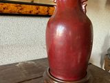 un vase rouge posé sur une table en bois, avec un miroir en arrière-plan