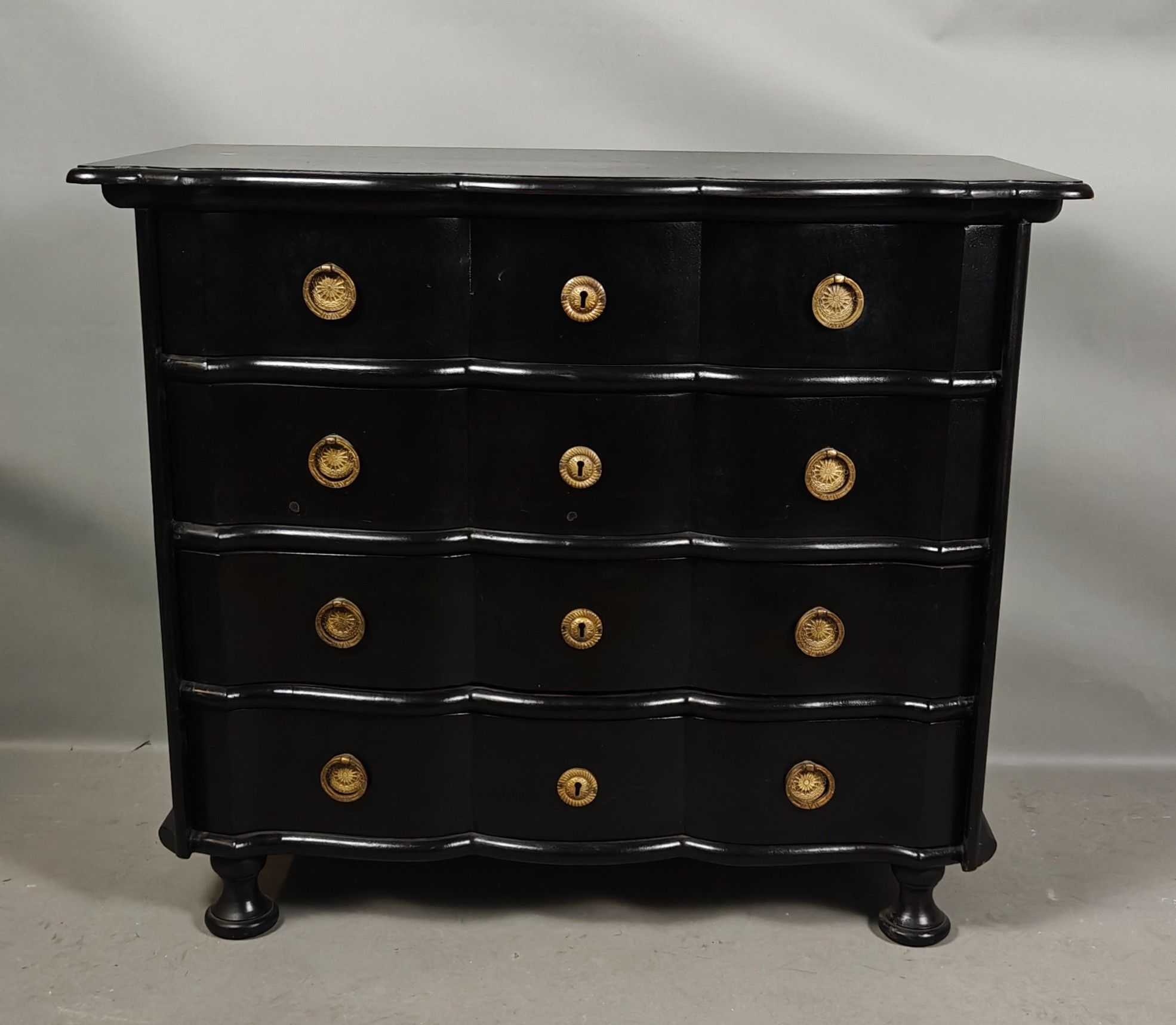Commode en bois laqué noir, à façade mouvementée, ouvrant à …