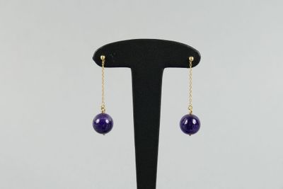 une paire de boucles d'oreilles ornées de perles violettes, suspendues à un support noir
