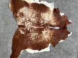 une peau de vache brune et blanche posée par terre